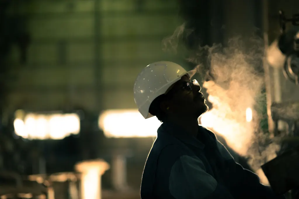 Operador de capacete e óculos olhando para o alto numa planta industrial com vapor