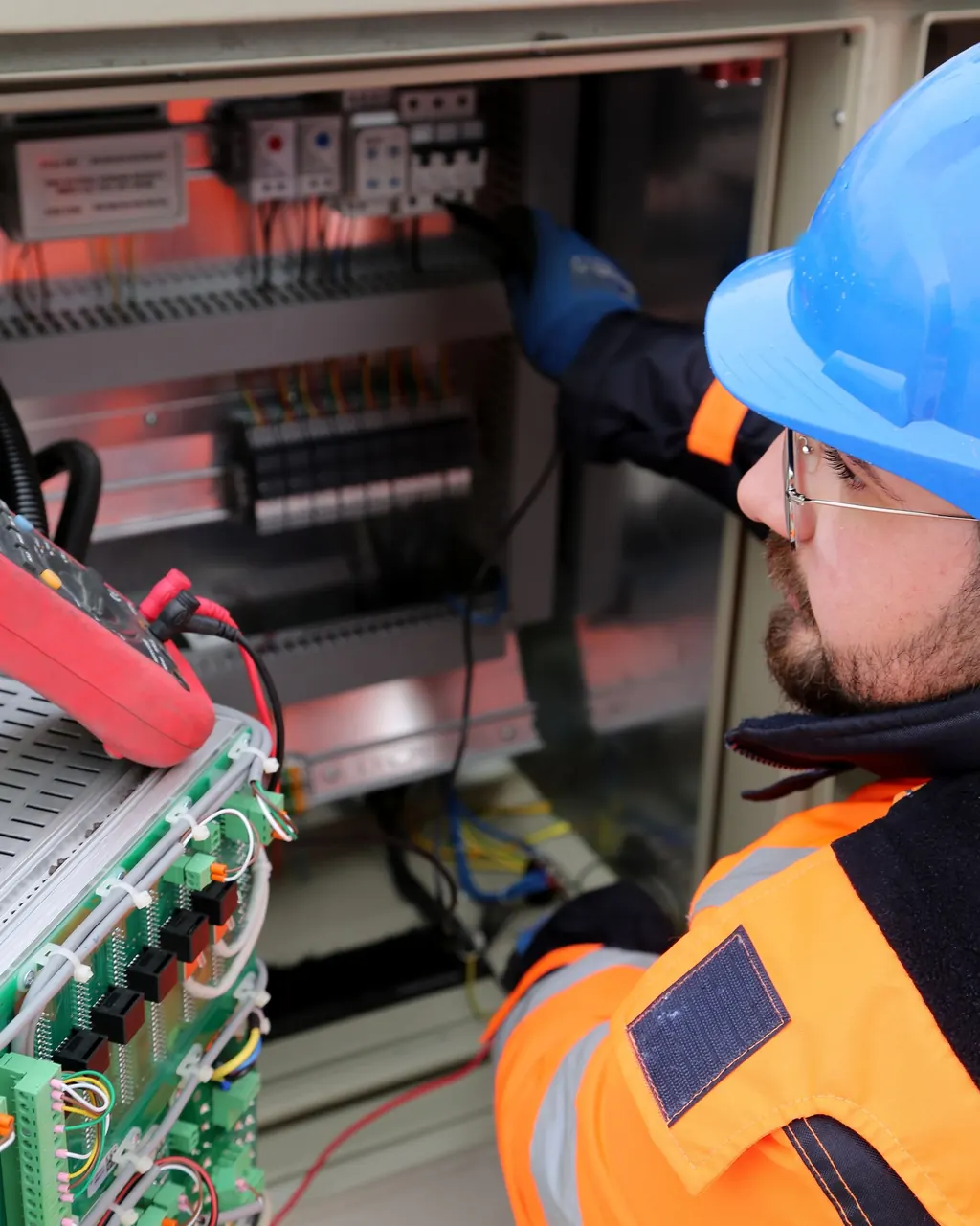 Eletricista de capacete e luvas fazendo a manutenção de um painel elétrico