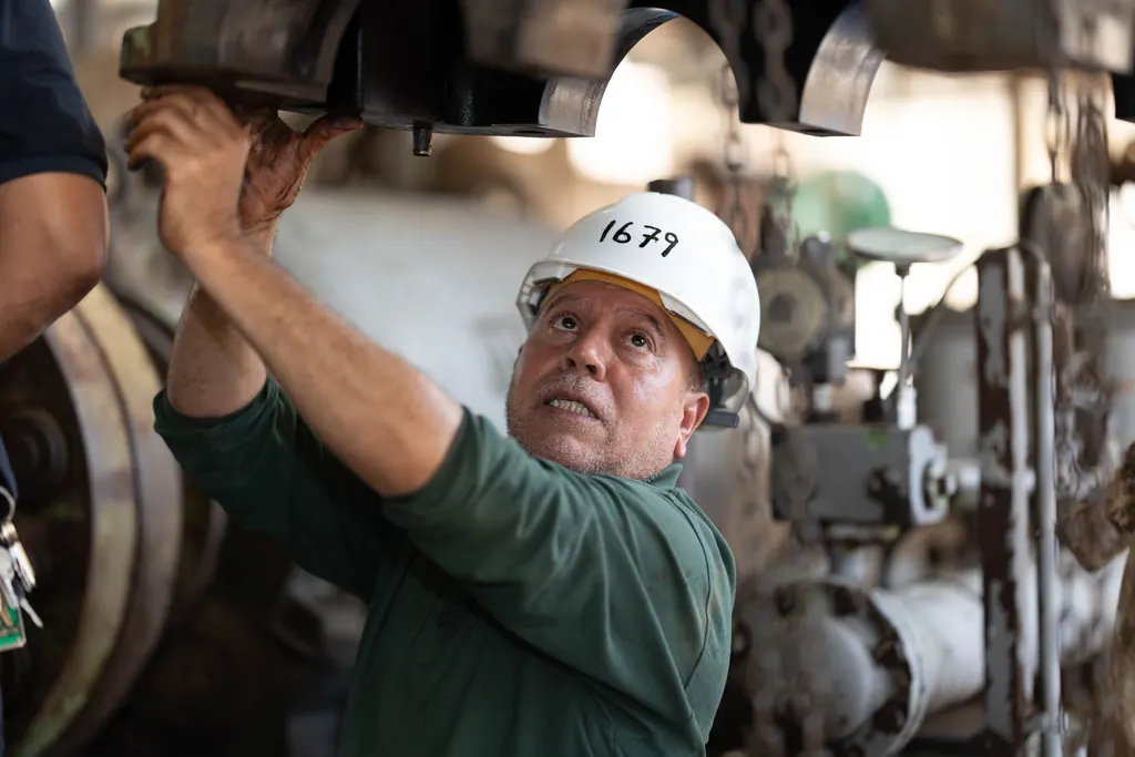 Mecânico de capacete encaixando uma peça pesada numa máquina industrial