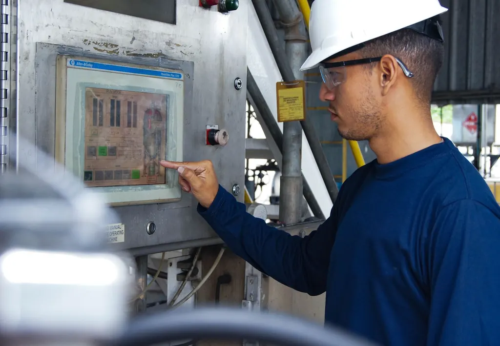 Técnico de capacete e óculos operando o painel de controle de uma planta industrial